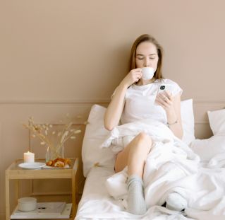 Woman Drinking from a Mug While Sitting on the Bed