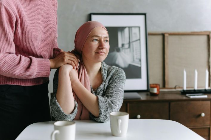 A supportive moment indoors featuring a cancer patient comforted by a friend, conveying emotion and care.