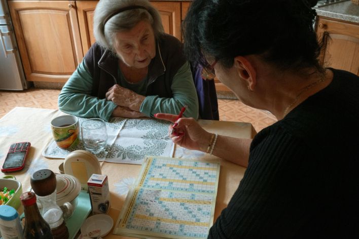 A senior woman and her caregiver work together on a crossword puzzle in a cozy kitchen.