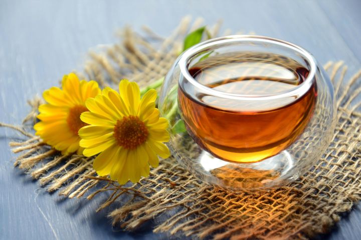 Glass cup of herbal tea with yellow flowers on a textured background.