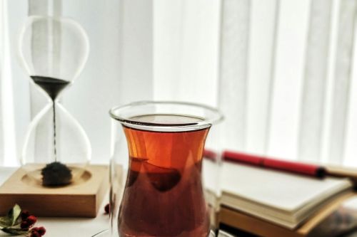 A stylish glass of tea with an hourglass and books on a light-filled table setting.