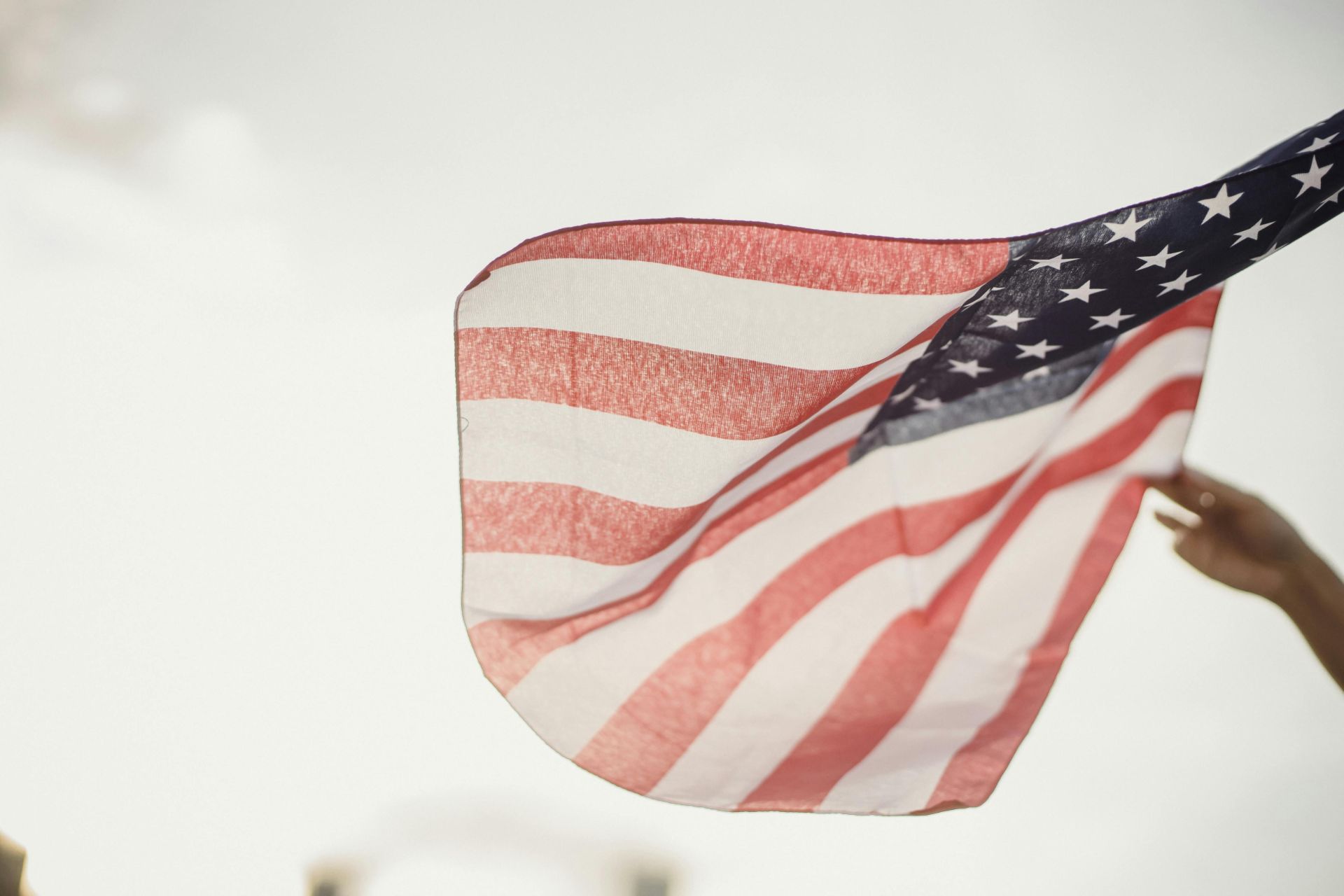 An American flag waving in the air held by a person's hand, symbolizing freedom and patriotism.