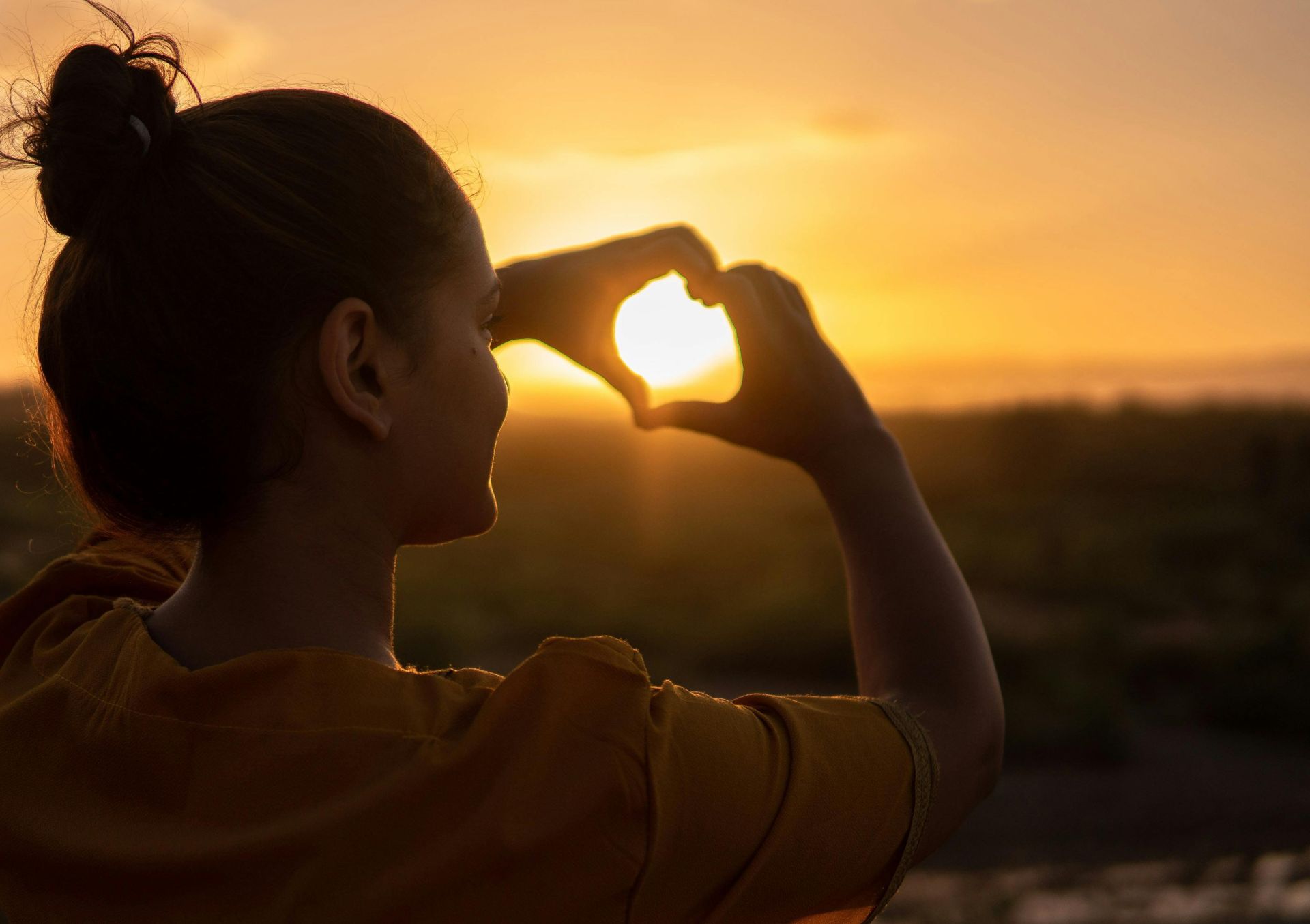 A silhouette of a young woman forming a heart shape at sunset in Kelâat M'Gouna, Morocco.
