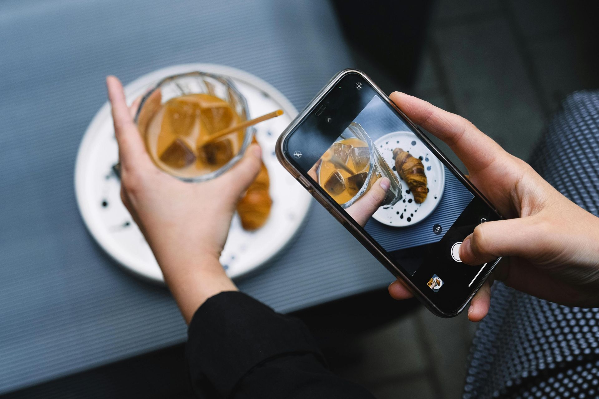 Hands taking a photo of iced coffee and croissant with a smartphone, perfect for food bloggers.