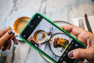 A smartphone captures a delicious coffee and dessert moment in a cozy restaurant.