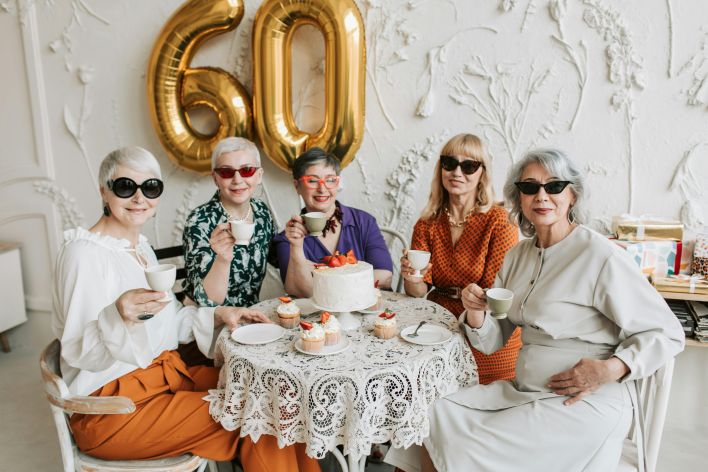 A joyful gathering of senior women celebrating a 60th birthday with tea and cake.