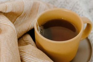 Yellow cup of tea with a teabag nestled in warm, patterned textiles portraying a cozy atmosphere.