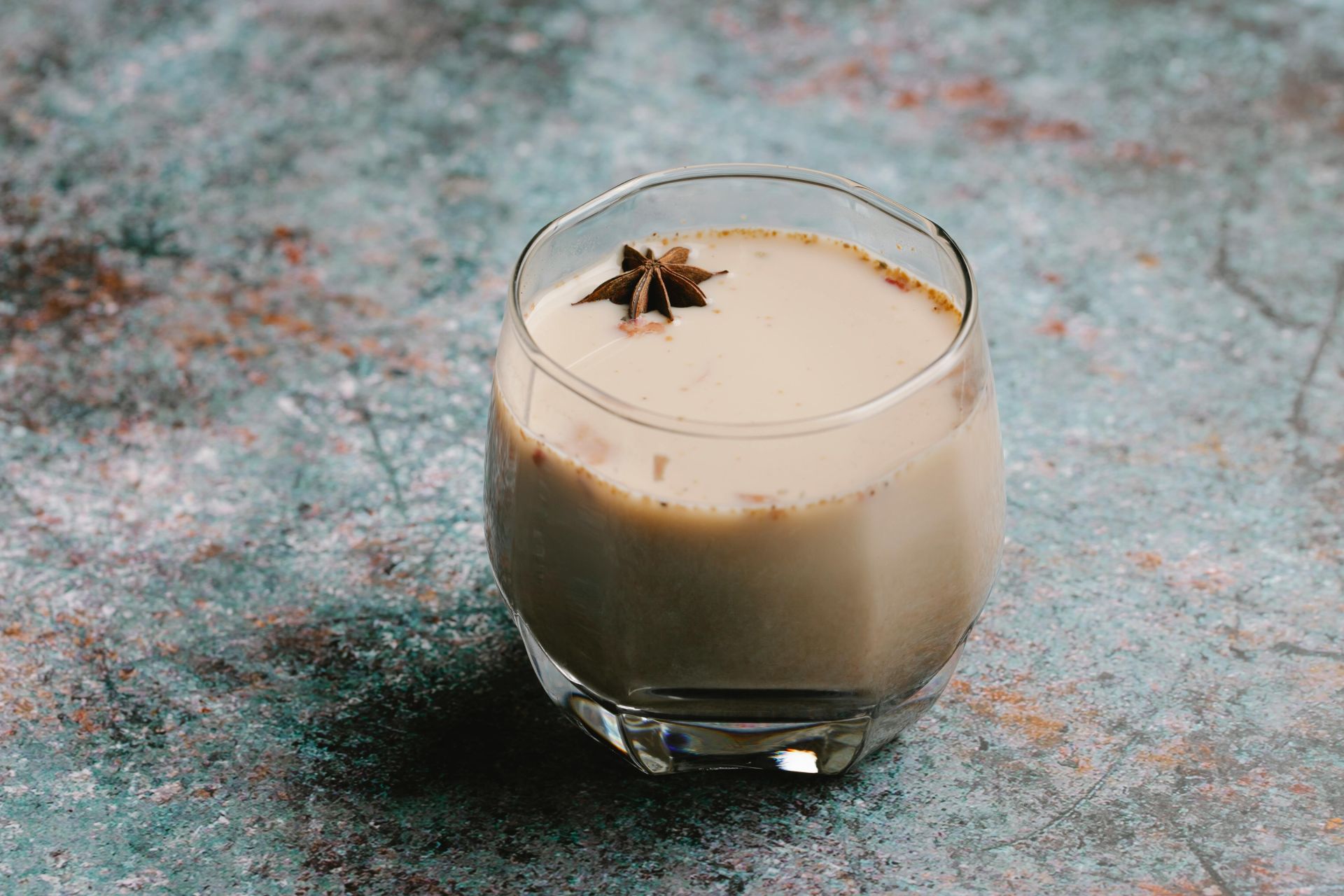 A clear glass of chocolately chai tea with a star anise floating on top